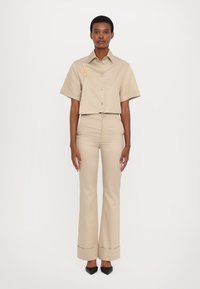 Beige cropped shirt with short sleeves and button closure, paired with beige flared pants, featuring a folded hem. Black pointed shoes.
