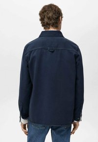 Navy blue shirt jacket with a relaxed fit, buttoned cuffs, and a point collar; features a loop at the back for hanging, made from textured fabric.