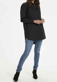 Sort skjorte med lange ærmer, rund kant og sideslidser, parret med tætsiddende blå jeans og sorte ankelstøvler.