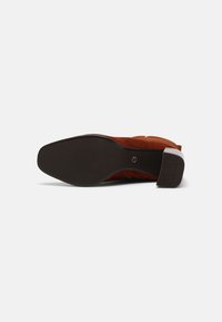 Vue unique d'une botte cheville en daim marron avec une semelle extérieure noire lisse et un petit talon bloc présentant un motif antidérapant.