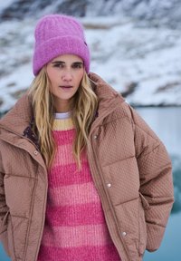 Hnedá prešívaná bunda, žiarivo ružový a žltý pruhovaný pletený sveter a huňatá ružová čiapka. Hladké textúry na pozadí snehu.