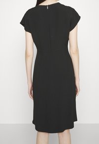 Svart klänning med korta ärmar, rund halsringning och dold dragkedja i ryggen. Slät tyg med en lätt lyster, knälång längd.