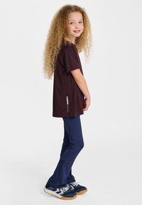 Czerwono-bordowa koszulka z krótkim rękawem z logo po stronie, zestawiona z granatowymi legginsami i granatowymi butami sportowymi z akcentami w odcieniach szarości i bieli.