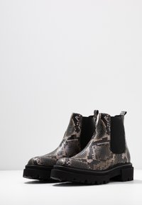 Botas Chelsea de plataforma negras con un patrón de piel de serpiente, que cuentan con una parte superior de textura suave, una suela de goma resistente y paneles laterales elásticos.