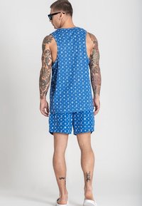 Modrý športový top a šortky, vyrobené z ľahkej tkaniny, s bielym vzorom loga, vo voľnom strihu a hladkej textúre.