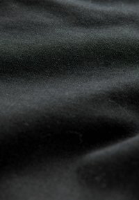 El tejido negro tiene una textura suave con fibras mínimamente visibles. La tela está ligeramente arrugada, mostrando sus cualidades de caído.