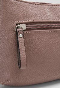Sac en cuir texturé rose avec une poche zippée à l'avant, en métal argenté et un passepoil noir contrastant le long de la fermeture éclair et des bords latéraux.