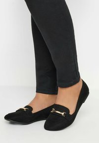 Ballerine nere in suede con punta affusolata, dotate di un accento in metallo dorato e design slip-on. Abbinate a jeans neri aderenti.