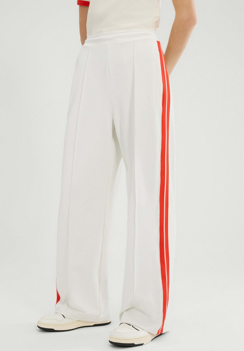 Pantalones anchos blancos con rayas rojas a los lados, que presentan un diseño plisado y una textura suave y lisa. Con bolsillos laterales.