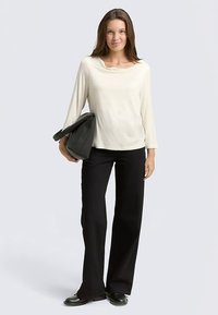 Light cream long-sleeve top with a cowl neckline, paired with black wide-leg pants and black shoes, holding a black handbag.