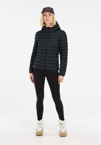 Zwarte pufferjack met een rits aan de voorkant, met een horizontaal gestikt ontwerp. Gecombineerd met zwarte leggings en tan laarzen met een binnenvoering van bont.