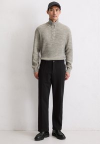 Un pull zippé gris en tricot avec un col haut, associé à un pantalon noir à jambes droites et des chaussures noires à lacets. Design simple sans motifs visibles.