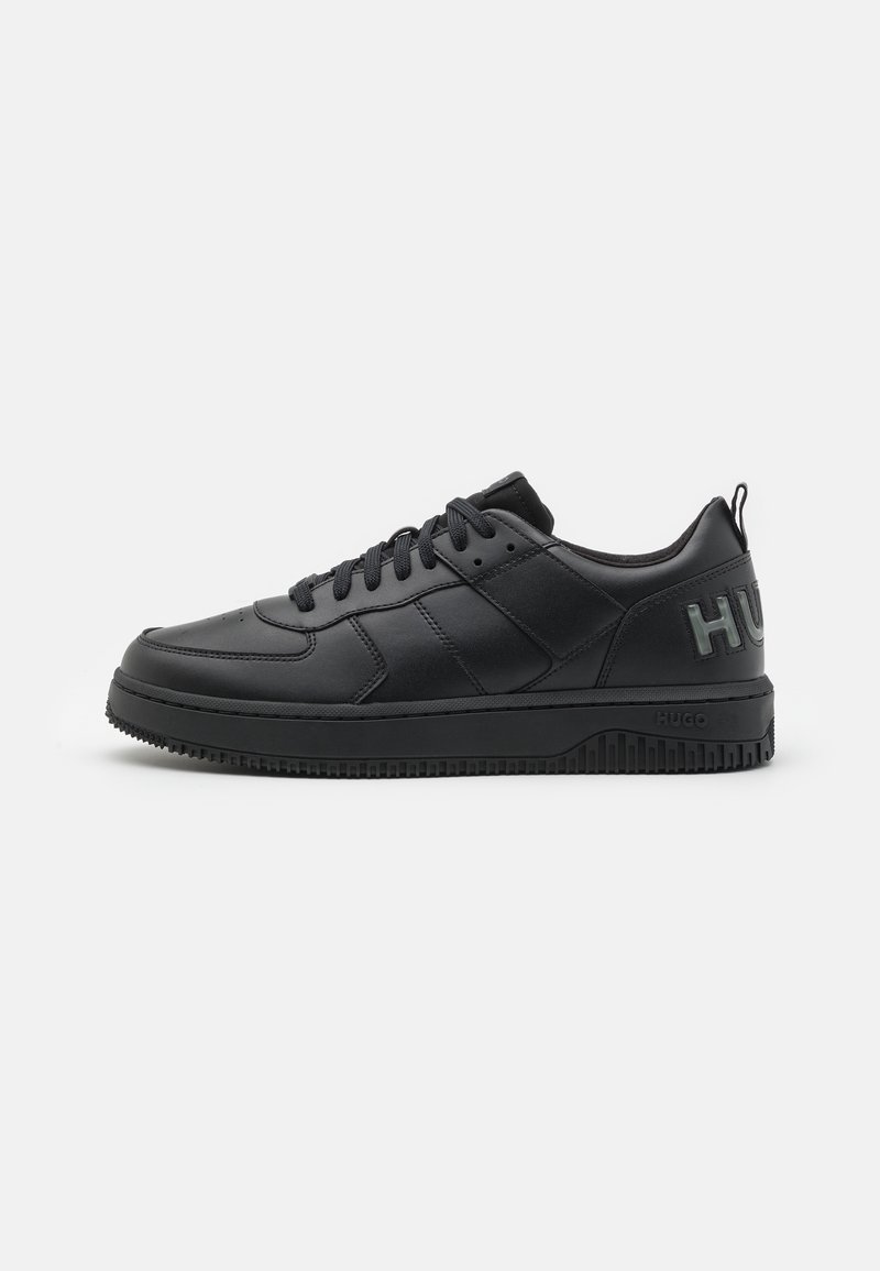 Sneaker in pelle nera con punta rotonda, lacci piatti e suola in gomma testurizzata. Presenta il logo "HUGO" impresso sul tallone.