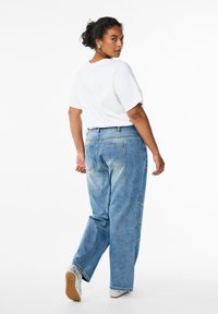 Ljusblå denimjeans med en avslappnad passform, fem fickor och synliga sömnadsdetaljer, i kombination med en vanlig vit t-shirt och sneakers.