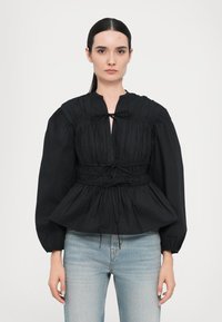 Svart bluse med samlet tekstur, nøkkelhullkrage og snorjustert midje. Lange ermer med elastiske mansjetter. Kombinert med lys denim.