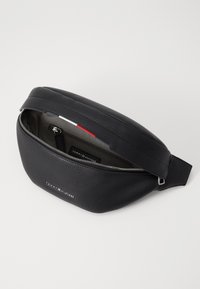 Black leather fanny pack with a textured finish, silver zipper, and logo detailing. Open top reveals an interior compartment with organizational pockets.