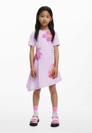 Rochie mov cu imprimeuri florale mari în nuanțe de roz și galben. Marginea este asimetrică. Modelul poartă șosete roz și sandale negre.