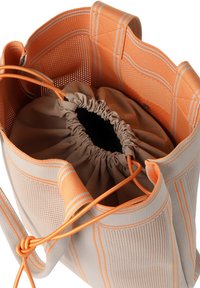 Trekzak met een ademende oranje gaas buitenkant en een beige voering, met oranje accenten en een gather-top voor een veilige sluiting.