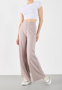 Helle rosa, gerippte, weit geschnittene Hose mit hoher Taille. Kombiniert mit einem weißen, figurbetonten, kurzärmligen Cropped-Top und beigen Sneakern.