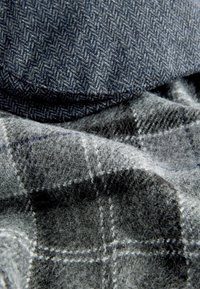 Close-up of two overlapping wool fabrics, one dark blue with herringbone pattern and one grey with plaid pattern.