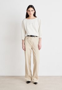 Crème-kleurige, ontspannen trui met een bootnek en pofmouwen, gecombineerd met beige, wijduitlopende broeken en zwarte, puntige schoenen.