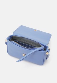 Ljusblå läderhandväska med guldfärgad hårdvara, zippered inredning och en framflikslåsning. Insidan har flera fack.