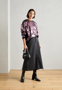 Suéter negro con lentejuelas, falda larga de mezclilla negra, botas negras hasta la rodilla y pequeño bolso negro con herrajes plateados.