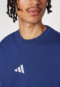 T-shirt en coton bleu marine avec un col rond et un logo Adidas blanc sur le côté gauche. Texture douce et coupe standard.