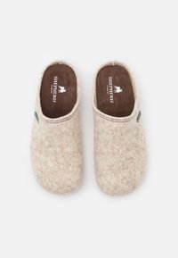Chaussons en feutre beige clair avec une texture douce, dotés d'un dos ouvert et d'une semelle intérieure marron foncé portant le logo "Shepherd" visible.