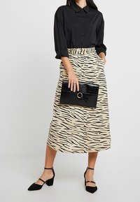 Černá košile na knoflíky, béžová sukně s černými tygřími pruhy, černá kabelka s krokodýlí texturou a černé lodičky s kotníkovými pásky.