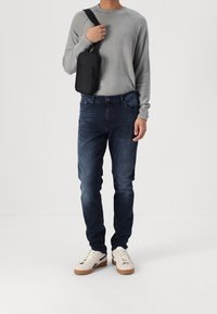 Grå texturerad långärmad tröja, mörkblå jeans, vita sneakers med svarta accenter och en liten svart axelremsa.