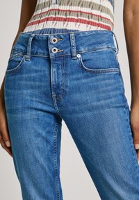 Blå denimjeans med hög midja, med en dubbelknäppning, två framsidans fickor och en mjuk textur.