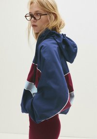 Sweat à capuche bleu marine avec des rayures bordeaux et bleu clair, doté d'une capuche avec cordon de serrage et d'une coupe ample. Fabriqué en tissu léger et doux.