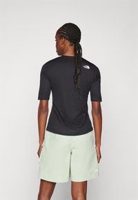 Svart kortärmad skjorta med logotyp på ryggen, kombinerad med ljusgröna shorts med sidofickor. Slät tygkvalitet med ledig passform.