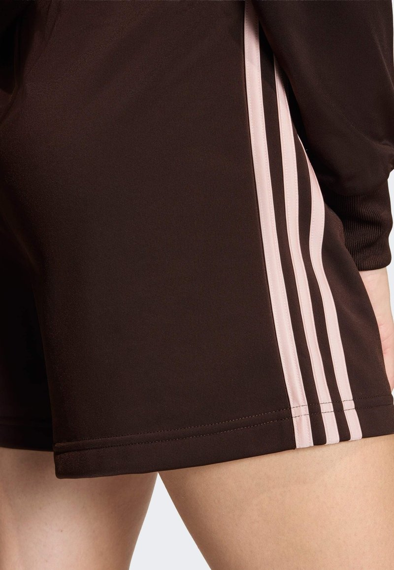 Brown athletic shorts featuring three vertical pink stripes on the side, made from a smooth fabric with a clean hem finish.