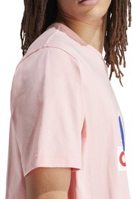 Helles rosa Baumwoll-T-Shirt mit kurzen Ärmeln, das auf der Vorderseite ein großes rot-blaues Grafikdesign und einen runden Ausschnitt aufweist.