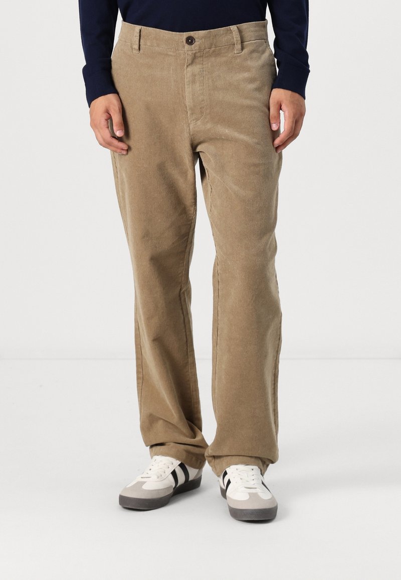 Beige corduroy broek met een recht model, voorzien van een knoopsluiting en steekzakken aan de voorkant, gecombineerd met witte en grijze sneakers.