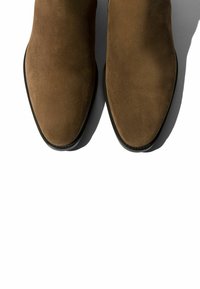 Botas de tobillo de ante marrón con punteras afiladas y suelas negras, con una textura suave y un diseño limpio. Sin hardware ni acentos visibles.