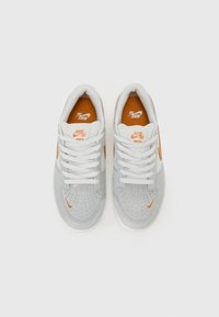 Sapatos Nike SB em camurça e malha cinza claro. Apresentam detalhes em laranja, atacadores brancos e um padrão perfurado na caixa dos dedos.