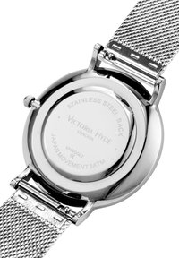 Montre en acier inoxydable avec un boîtier argenté poli et un bracelet en maille. Le dos présente des détails gravés de la marque et du mouvement, résistance à l'eau de 3 ATM.