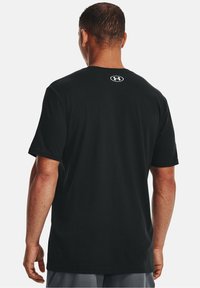 T-shirt nera in cotone con collo a giro, maniche corte e un logo più piccolo bianco sul retro alto. Tessuto morbido e vestibilità comoda.