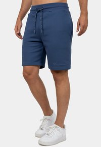 Blauwe heren shorts gemaakt van zachte stof, met een elastische tailleband met trekkoord en zijzakken. Eenvoudig ontwerp met subtiele branding.