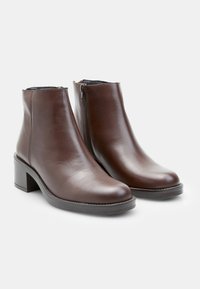 Stivaletti in pelle marrone con punta rotonda, tacco a blocco e zip laterale. Texture liscia con delicate cuciture lungo la suola.