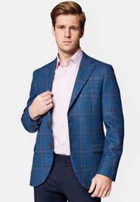 Niebieska marynarka w kratę wykonana z teksturowanej tkaniny, z dopasowanym krojem, dwiema guzikami i brązowymi akcentami. Założona na jasnoróżową koszulę.