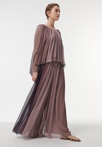 Vestido fluido y con volantes en un suave tono malva y de tela transparente color ciruela profundo, con delicados acentos de perlas a lo largo del costado y largas mangas amplias.