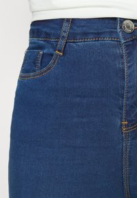 Höga mörk denimjeans med orange sömmar, en sidficka och metallknappstängning, med en slät textur och figursydd passform.
