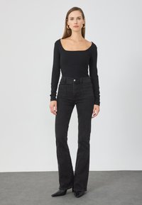 Schwarzes, geripptes Langarmoberteil mit quadratischem Ausschnitt, kombiniert mit hochgeschnittenen schwarzen Jeans mit weit ausgestelltem Bein und zwei Gesäßtaschen.