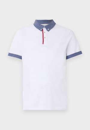 Tricou polo alb cu mâneci scurte, guler albastru cu nasturi, manșete albastre și o dungă verticală roșie de-a lungul fantei cu nasturi.