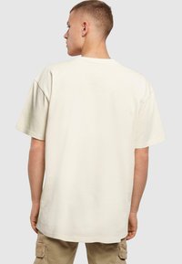 Creme oversized T-shirt lavet af bomuld, med korte ærmer, rund halsudskæring og en afslappet pasform, båret med beige cargobukser.