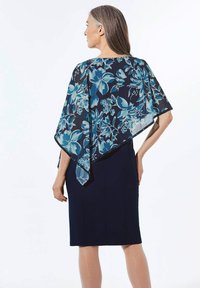 Blumenmuster-Schal in Blau- und Türkistönen über einem eleganten schwarzen Kleid. Leichter, transparenter Stoff fällt weich.